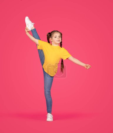 Photo for Sporty little girl making gymnastic exercises, flexible preteen female child raising her leg in twine and looking at camera, doing stretching and posing over pink studio background, full length - Royalty Free Image