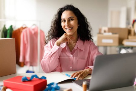 Photo for Owning Clothing Store. Smiling Middle Eastern Woman Designer Using Laptop Computer Posing At Workplace In Modern Shop Office, Smiling To Camera. Lady Having Fashion Business. Ecommerce And Retail - Royalty Free Image