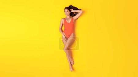 Foto de Relajación de verano. Vista superior de Happy Lady tomando el sol en naranja traje de baño de una pieza acostado sobre fondo amarillo, Studio Shot. Fiesta en la piscina y traje de baño oferta de moda. Panorama - Imagen libre de derechos