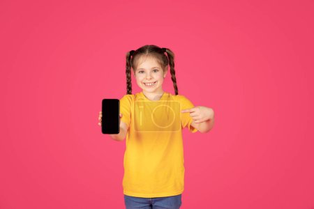 Photo for Cute Preteen Girl Pointing At Smartphone With Blank Screen In Hand, Cheerful Female Child Advertising New Mobile Application Or Website, Standing Isolated Over Pink Background, Mockup Image - Royalty Free Image