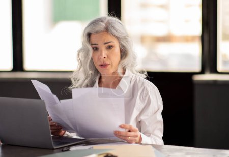 Photo for Headhunting Problems And Difficulties. Confused Businesswoman Looking Through Paper Documents And Bills, Reading Bad News Sitting Near Laptop In Office Interior. Entrepreneurship Paperwork Issues - Royalty Free Image
