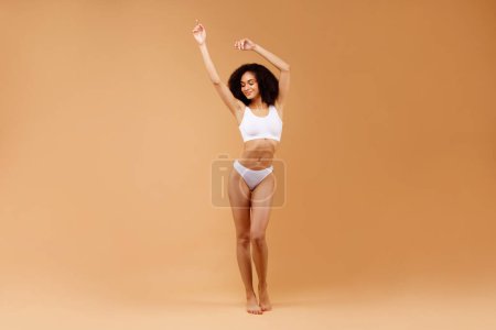 Téléchargez les photos : Concept minceur. Heureuse dame sexy avec une forme de corps idéale posant en sous-vêtements blancs sur fond de studio beige, espace de copie pour la publicité, bannière, plan complet - en image libre de droit