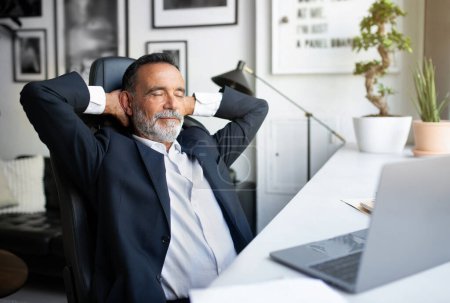 Photo for Happy relaxed european senior businessman in suit and closes eyes resting alone at table with computer in office interior. Break from work, business remotely, gadget, ad and offer - Royalty Free Image