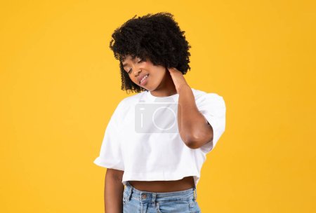 Photo for Unhappy tired millennial african american curly woman in white t-shirt massaging her neck, suffering from muscle pain, isolated on yellow studio background. Health problems, overwork, spasm - Royalty Free Image