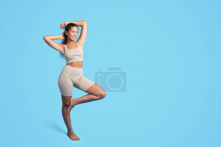 Photo for Positive millennial caucasian slim woman in sportswear enjoy workout result, isolated on blue studio background, full length. Sports, fitness, weight loss and body care at gym or home - Royalty Free Image