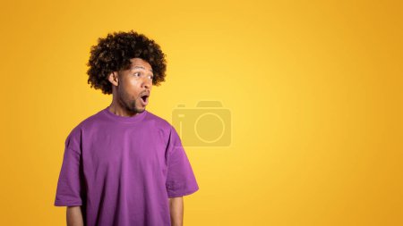 Foto de Alegre sorprendido hombre rizado adulto negro en camiseta púrpura con la boca abierta se ve en el espacio vacío sobre fondo naranja, estudio, panorama. Sorpresa, grandes noticias, venta, anuncio y oferta - Imagen libre de derechos