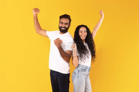 Téléchargez les photos : Les gagnants. Joyeux couple arabe secouant les poings souriant à la caméra, posant Célébration des réalisations et du succès ensemble sur fond de studio jaune. Joie et concept de célébration de la victoire - en image libre de droit