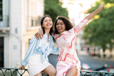 Foto de Retrato de dos amigas multiraciales riéndose juntas al aire libre, jóvenes mujeres felices abrazando y mirando a la cámara, divirtiéndose mientras caminan por la calle de la ciudad en verano, espacio libre - Imagen libre de derechos