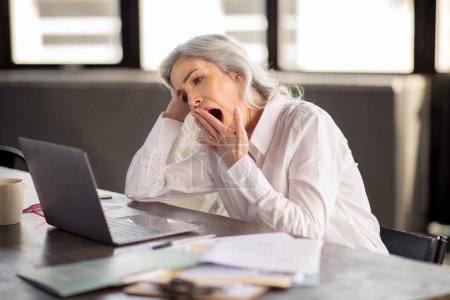 Photo for Fatigue Issue. Bored Middle Aged Businesswoman Yawning Looking At Laptop Computer, Tired Of Office Work Routine Sitting At Workplace Indoor. Manager Lady Strugging With Boring Business Tasks - Royalty Free Image