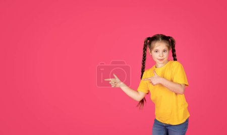 Foto de Bonita oferta. Pretty Little Girl señalando a un lado con dos dedos, sonriendo lindo niño preadolescente femenino demostrando espacio de copia para el diseño de publicidad sobre fondo de estudio rosa, Panorama - Imagen libre de derechos