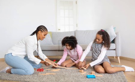 Photo for Happy African American Mom And Two Daughters Playing Together With Toy Railway Having Fun On Weekend, Sitting On Floor In Cozy Modern Living Room. Mommy Enjoying Pastime With Preteen Kids At Home - Royalty Free Image