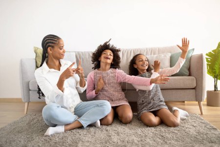 Photo for Domestic Happiness. Funny Black Mom And Her Daughters Posing Having Fun Sitting On Floor In Living Room At Home. Family Bonding Spending Weekend Indoors, Laughing And Fooling Together - Royalty Free Image