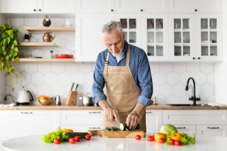 Photo for Happy senior man preparing healthy food in kitchen interior, smiling elderly gentleman cooking vegetarian lunch or dinner at home, mature male wearing apron chopping vegetables, copy space - Royalty Free Image