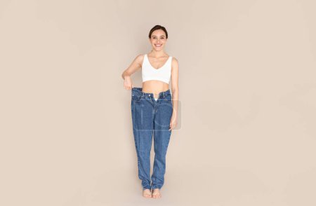Photo for Diet, healthy lifestyle, slimming concept. Cheerful slim beautiful young woman wearing big jeans after weight loss diet program on beige studio background, panorama with copy space - Royalty Free Image