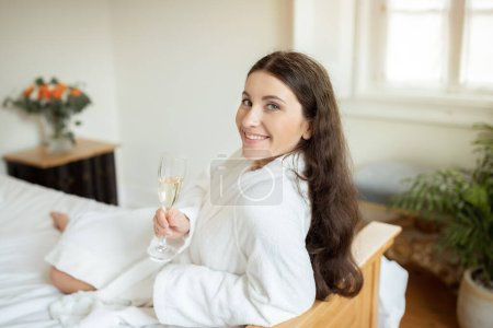 Photo for Luxury Vacation. Smiling Young Lady Enjoying Sparkling Wine, Holding Champagne Glass And Tasting Luxurious Alcohol Drink At Cozy Hotel Interior. Woman On Vacation Resting On Bed Indoor - Royalty Free Image