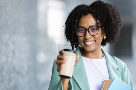 Photo for Portrait of pretty curly cheerful young black lady in beautiful fornal outwear employee posing outdoors next to office building, holding notepads and paper cup, drinking coffee, copy space, closeup - Royalty Free Image