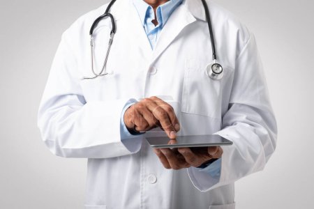 Photo for Caucasian mature man doctor in white coat typing on tablet, isolated on gray background, studio, close up. Medicine service, app for disease treatment, diagnostics, health care, ad and offer - Royalty Free Image