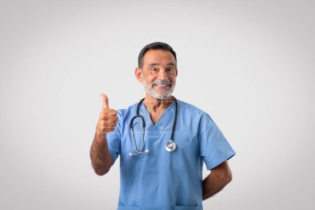 Photo for Positive caucasian mature doctor in uniform show thumb up, recommend medicine service, isolated on gray background, studio. Disease treatment, health care and surgery, help and good result - Royalty Free Image