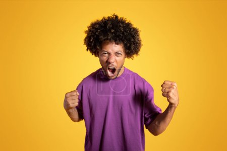 Téléchargez les photos : En colère agressif mécontent noir adulte bouclé homme en t-shirt violet avec bouche ouverte criant, isolé sur fond orange, studio. Mauvaises nouvelles, émotions, stress, publicité et offre - en image libre de droit