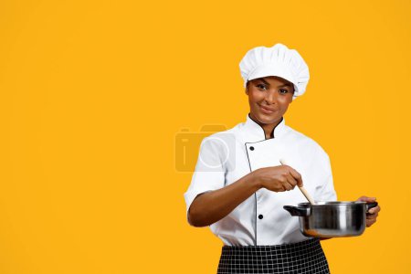 Photo for Culinary Concept. Smiling black female chef in toque holding saucepan and looking at camera, beautiful young african american cooker lady preparing food while standing over yellow background - Royalty Free Image