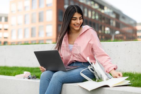 Lächelnde Studentin, die mit Arbeitsbüchern und Laptop lernt, Frau, die Bücher liest und Computer benutzt, während sie im Park oder auf dem College-Campus im Freien sitzt, freier Raum
