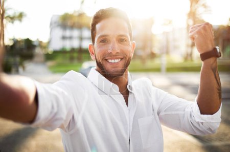 Téléchargez les photos : Homme d'affaires européen heureux en chemise prendre selfie et secouer le poing tout en se tenant à l'extérieur, souriant et capturant moment de nouveau lieu de travail - en image libre de droit
