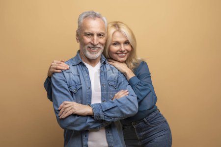 Téléchargez les photos : Studio portrait de occasionnels beaux amis couples âgés posant sur fond beige, heureux sénior beau barbu aux cheveux gris homme et jolie femme blonde embrassant, souriant à la caméra - en image libre de droit