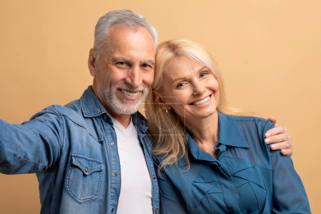 Téléchargez les photos : Joyeux beau couple deux amis âgés homme aux cheveux gris femme blonde en denim vêtements décontractés étreignant, prenant selfie ensemble, isolé sur fond de couleur pastel, portrait studio - en image libre de droit