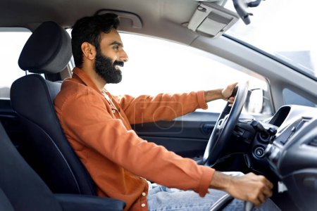 Foto de Propio auto. Vista lateral del alegre hombre de Oriente Medio conduciendo cómodo auto sentado en el lujoso interior del automóvil. Guapo barbudo hombre de negocios que va a la oficina en automóvil - Imagen libre de derechos