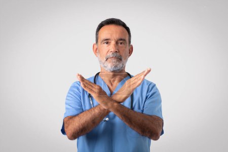 Photo for Serious caucasian senior doctor surgeon in blue uniform crossed arms, making stop sign, isolated on gray background, studio. Refusal, say no, disease control medicine, health care - Royalty Free Image