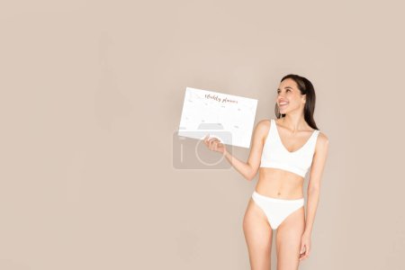 Photo for Happy cheerful young brunette woman demonstrates periods calendar, isolated on beige studio background, copy space. Women healthcare, menstruation, menstrual cycle concept, mobile app - Royalty Free Image