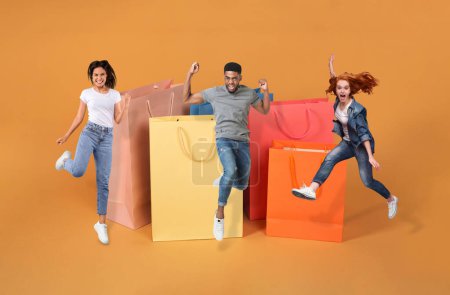 Photo for Thrilled multiracial young people celebrating black friday sales, collage. Happy emotional millennial man and women jumping in the air over orange background next to huge shopping bags - Royalty Free Image