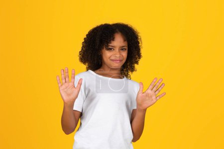 Photo for Dissatisfied curly teenager black schoolgirl in white t-shirt making disgust sign, stop isolated on yellow background, studio. Problems, aversion, study, knowledge, ad and offer - Royalty Free Image