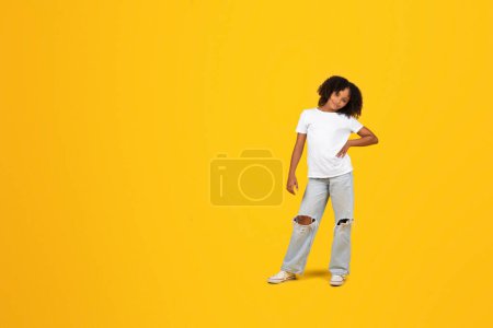Photo for Happy confident curly teenager black schoolgirl in white t-shirt look at camera, isolated on yellow background, studio, full length. Study, knowledge, lifestyle fashion, ad and offer - Royalty Free Image