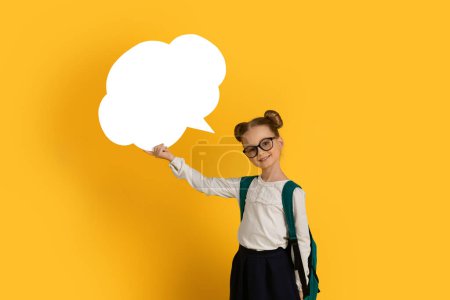 Photo for Cute Little Schoolgirl With Empty Speech Bubble In Hand Posing On Yellow Background In Studio, Smiling Preteen Female Child Wearing Backpack Showing Copy Space For Advertisement, Mockup - Royalty Free Image