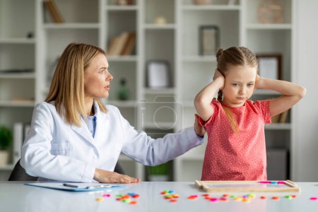 Photo for Supportive Psychotherapy. Therapist Woman Comforting Offended Little Girl During Meeting In Office, Stubborn Small Female Child Covering Ears With Hands, Ignoring Psychologist Lady, Closeup - Royalty Free Image