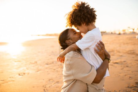 Téléchargez les photos : Connexion mère-fils. Aimant mère afro-américaine et son fils coller à l'extérieur tout en marchant au bord de la mer, copier l'espace, vue de côté. Concept de famille heureuse - en image libre de droit