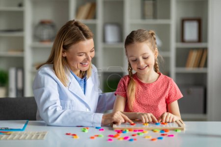 Photo for Child development specialist lady working with cute little girl, making words from colorful plastic letters together during therapy session, therapist lady making development activities with kid - Royalty Free Image