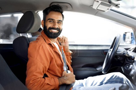 Foto de Automóvil nuevo. Smiling Middle Eastern Driver Man Fastening Seat Belt For Safety During Road Trip, Posing Looking At Camera In Own Auto (en inglés). Vehículo seguro y concepto de transporte - Imagen libre de derechos
