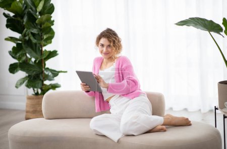 Photo for Technologies For Leisure. Happy Young Woman Using Digital Tablet At Home, Smiling Millennial Female Resting On Couch With Modern Gadget, Relaxing On Comfortable Sofa In Living Room Interior - Royalty Free Image