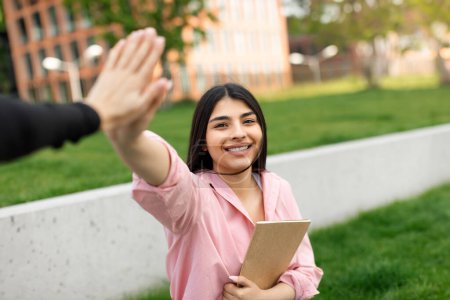 Photo for Happy smiling hispanic lady giving high five, celebrating academic success and passed exam, walking in college campus outdoors. Successful studentship concept - Royalty Free Image