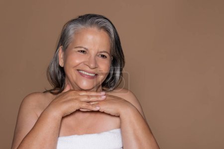 Foto de Sonriente señora europea de pelo gris senior disfrutar de frescura, belleza natural de la piel y el estilo de vida, aislado en el fondo del estudio beige. Higiena, fin de semana de spa y procedimientos rutinarios - Imagen libre de derechos