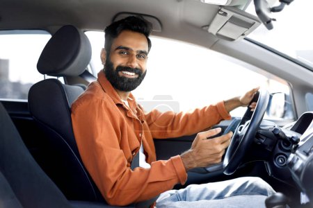 Foto de Aplicación de navegación del coche. Hombre conductor indio feliz usando teléfono móvil sentado en un automóvil nuevo, sonriendo a la cámara. Oriente Medio Guy conducción Websurf carretera y el uso de Gps Navigator Aplicación - Imagen libre de derechos