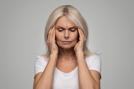 Photo for Headache Concept. Portrait of beautiful senior woman suffering from migraine, sick elderly female rubbing temples while standing over grey studio background, feeling unwell, having acute pain - Royalty Free Image