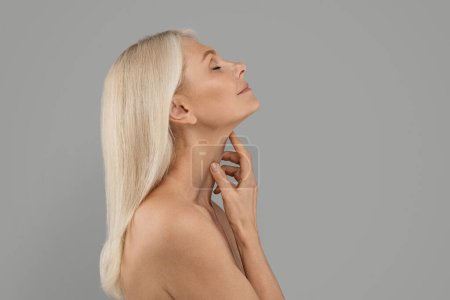 Photo for Double Chin Treatment. Beautiful Mature Woman Touching Soft Smooth Skin On Neck, Attractive Elderly Lady With Bare Shoulders Standing Over Light Grey Background, Enjoying Her Beauty, Copy Space - Royalty Free Image
