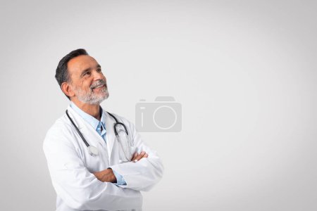 Photo for Glad confident caucasian mature doctor in white coat with crossed arms looks at copy space, isolated on gray background, studio. Advice, life insurance, health care, ad, offer, medicine in clinic - Royalty Free Image
