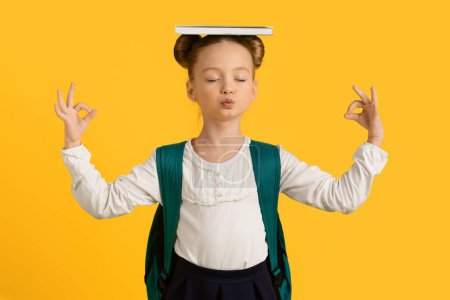 Photo for Keep Calm. Cute Little Schoolgirl Meditating With Book On Head And Closed Eyes, Adorable Female Child Coping With Learning Stress, Standing Isolated On Yellow Background, Copy Space - Royalty Free Image
