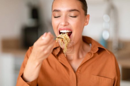 Photo for Home cooked delights. Woman eating delicious homemade pasta, enjoying tasty lunch with closed eyes while sitting at table in kitchen interior, closeup - Royalty Free Image