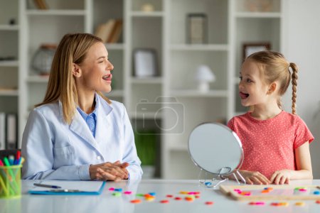 Photo for Child Specialist Making Tongue Exercises During Speech Therapy Session With Little Girl, Cute Preteen Female Kid With Stuttering Problem Having Meeting With Therapist Lady At Clinic, Closeup - Royalty Free Image