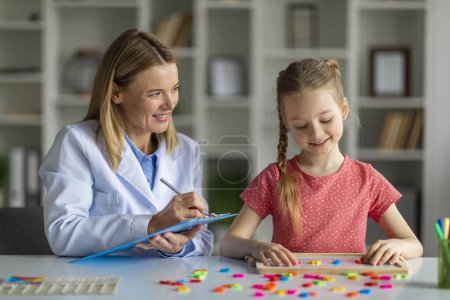 Photo for Assessment of kids mental development. Woman psychologist watching little girl playing with logical game, evaluating readiness for elementary school, child making words of colorful letters - Royalty Free Image